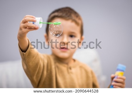Boy playing soap bubbles. Cute little boy at home blowing bubbles. Three years old child boy blowing bubbles. Happy childhood. Positive. Little boy with soap bubbles on grey background