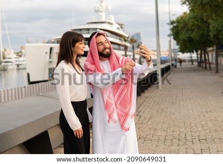 Smiling arab businessma taking selfie with his young attractive european female assistant in port
