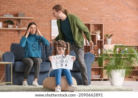 Little girl with torn picture of family and her quarreling parents at home
