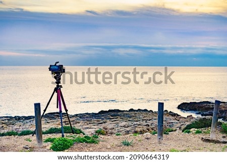 Professional camera on tripod taking picture film video of sunrise over sea.