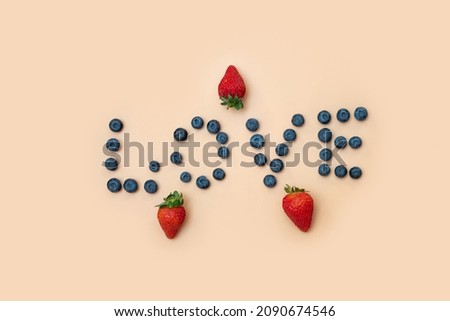 blueberries and strawberries on a beige background. The word "love" is laid out with berries in the center of the frame. the concept, the photo speaks about the love of berries