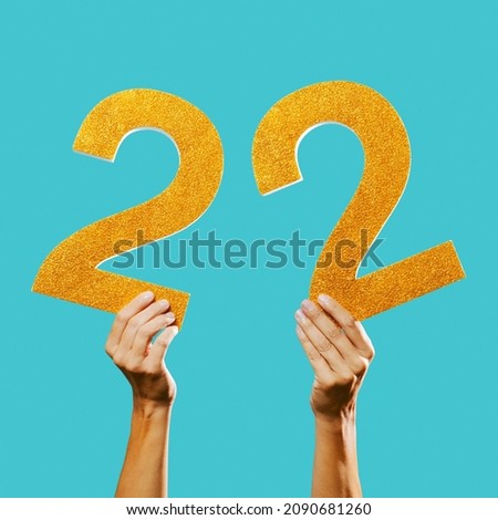 closeup of a man showing two golden three-dimensional numbers forming the number 22 on a blue background Royalty-Free Stock Photo #2090681260