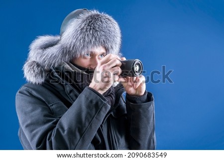 A man in winter clothes holds a camera in his hands. The photographer takes pictures of the beautiful winter. Snowfall.