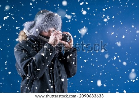 A man in winter clothes holds a camera in his hands. The photographer takes pictures of a beautiful winter. Snowfall. Photograph snow