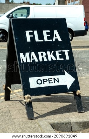 Black Flea Market sign stating that it is open and pointing the direction on a street