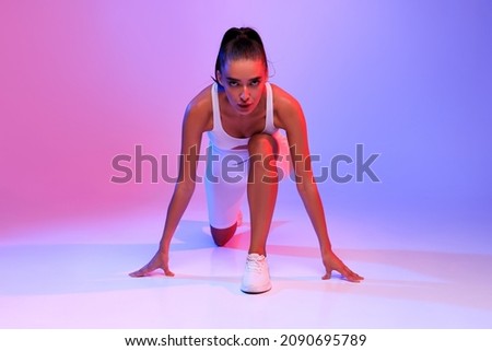 Front-View Of Motivated Female Runner Doing Crouch Start Looking At Camera Ready For Race Posing On Pink And Blue Neon Studio Background. Fit Woman Preparing For Running Workout Royalty-Free Stock Photo #2090695789