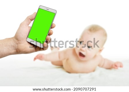parent hand taking photo of cute little baby in bed with smartphone, blank green chromakey screen