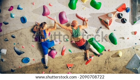 Two Experienced Rock Climbers Practicing Climbing on Bouldering Wall in a Gym. Friends Exercising at Indoor Fitness Facility, Doing Extreme Sport for Healthy Training. Giving Each Other High Five. Royalty-Free Stock Photo #2090708722