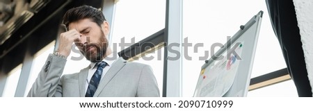 Low angle view of tired businessman in suit standing near flip chart in office, banner