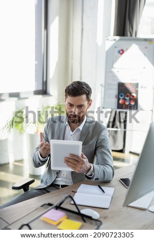 Businessman pointing at digital tablet near devices on working table in office