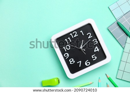 Stylish clock with stationery on color background