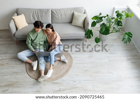 Young Asian couple using laptop together, surfing internet or watching movie online, sitting on floor in living room, top view. Millennial spouses using computer at home. Free space Royalty-Free Stock Photo #2090725465