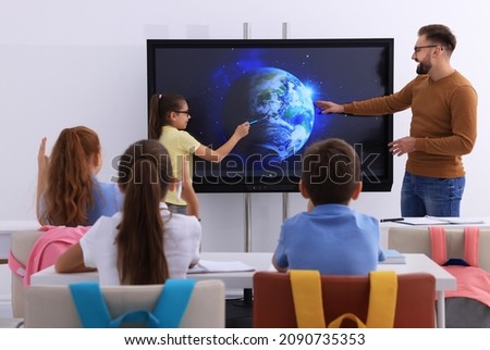 Teacher and pupil using interactive board in classroom during lesson Royalty-Free Stock Photo #2090735353