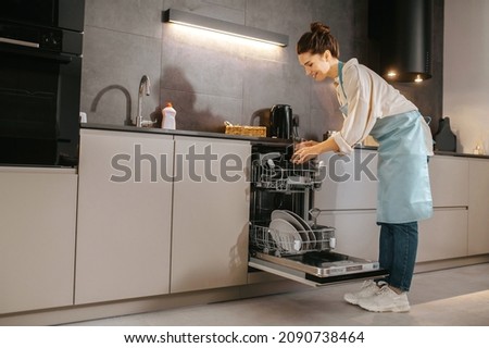 Young woman in the kitchen looking busy while washing the plates Royalty-Free Stock Photo #2090738464
