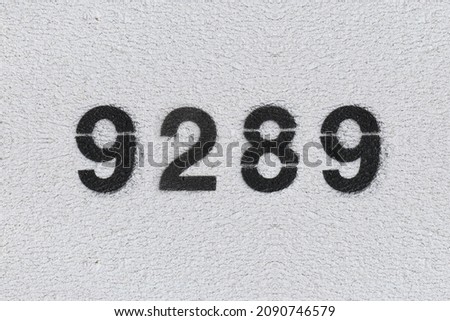 Black Number 9289 on the white wall. Spray paint. Number nine thousand two hundred and eighty nine.