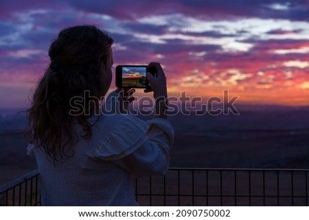 Back view beautiful little girl takes a picture of the amazing sunset.