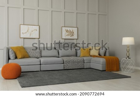 Comfortable large sofa with cushions and knitted blanket in living room