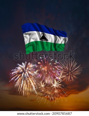 Holiday fireworks in evening sky and flag of Lesotho for National Independence day