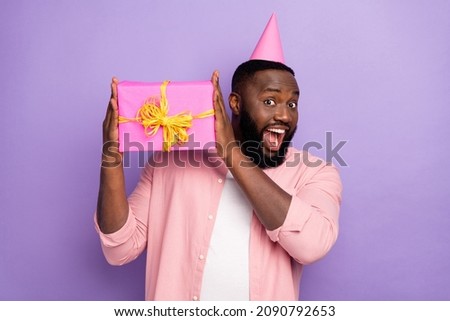 Photo of impressed young beard man hold present wear cap pastel shirt isolated on purple color background