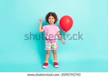 Full size photo of young little girl happy positive smile air balloons wave hello isolated over turquoise color background