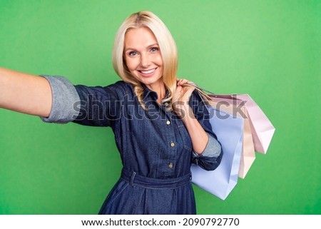 Photo of pretty adorable retired woman wear jeans clothes tacking selfie holding shoppers isolated green color background
