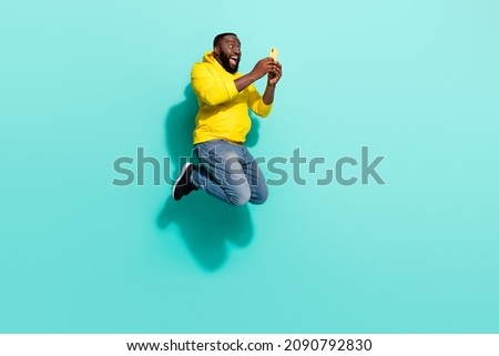 Full length photo of excited guy jump up use smartphone search bargain isolated over cyan color background
