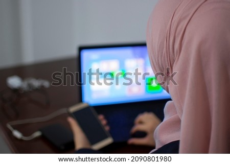 Muslim female student using laptop and mobile phone. Young girl study using technology devices. Online learning, corona virus pandemic lifestyle
