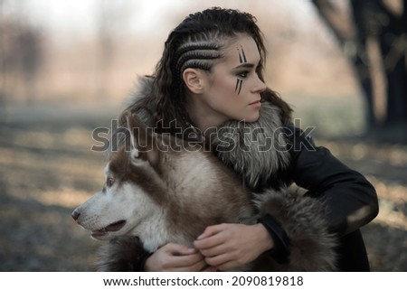 a girl with a belligerent make-up sits with a husky in the forest