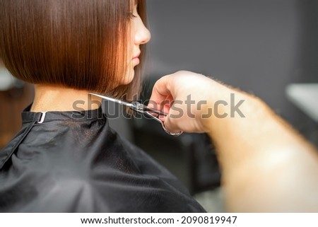 Woman having a new haircut. Male hairstylist cutting brown hair with scissors in a hair salon Royalty-Free Stock Photo #2090819947