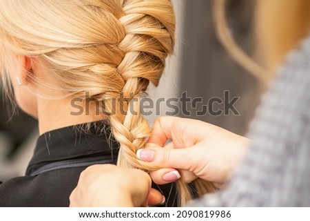 Braiding braid. Hands of female hairdresser braids long braid for a blonde woman in a hair salon Royalty-Free Stock Photo #2090819986