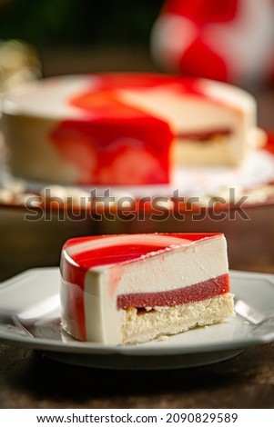Slice of a white and red french glazed strawberry cake on a red stand on a wooden table.