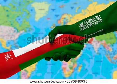 Handshake between Saudi Arabia and Oman flags painted on hands.With background of world map Royalty-Free Stock Photo #2090840938