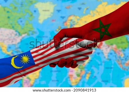 Handshake between Morocco and Malaysia flags painted on hands.With background of world map