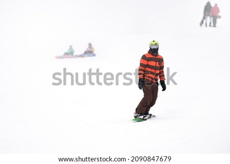 A snowboarder on a snowy mountainside. There is a blurry image of other snowboarders in the background. Selective focus. Copy space.                               