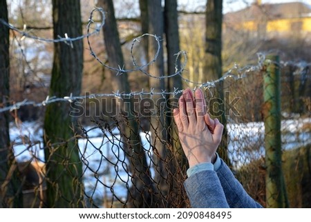 protesting woman with child and man. overcome the barbed wire, praying and gestures of supplication. indicating that they want freedom. tear down and damage the prison fence to cross the border line.