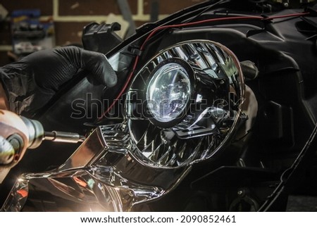 Car headlight in repair close-up. An auto mechanic wearing gloves installs the lens into the headlight housing. The concept of a car service.Installation of LED lenses in the headlight. LED lenses. Royalty-Free Stock Photo #2090852461