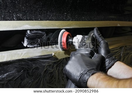 Car detailing - hands with an orbital polishing machine in an auto repair shop. Selective focus. A man polishes a car with a close-up grinder.