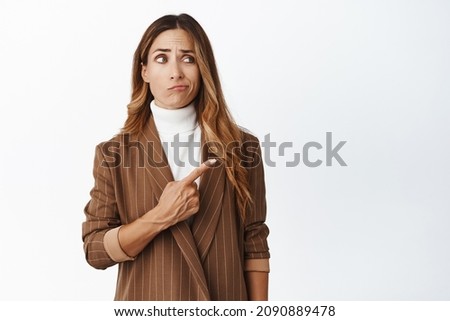 Skeptical adult ceo manager, female boss in company pointing right, looking with disappointed, unamused face expression, standing over white background