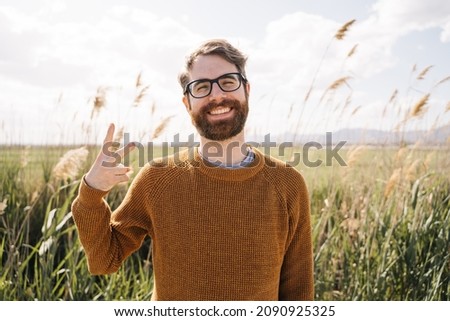 Happy young man with glasses and yellow sweater smiling and counting two with his fingers with a pampas field in the background. Nice and pleasant.