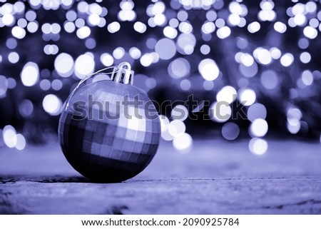 Festive New Year card in color 2022 very peri with free space for text. Christmas ball on a violet background with beautiful bokeh. Toned photo in a trendy violet color very peri, soft focus