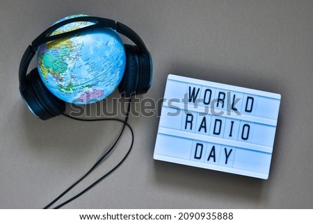 Light box with text WORLD RADIO DAY, globe and headphones on a beige background. World radio day. Top view, flat lay with copy space