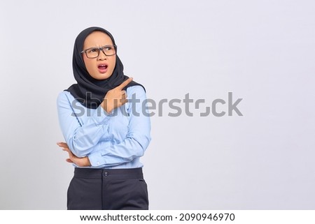 Portrait of shocked young Asian woman pointing finger at copy space isolated on white background