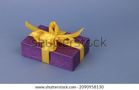 Dark blue paper box with yellow ribbon and bow on a light blue paper background. A festive concert. A gift box with a beautiful bow.