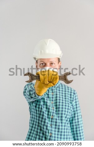 A female car mechanic holds a wrench in front of her at arm's length. Selective focus, vertical photo