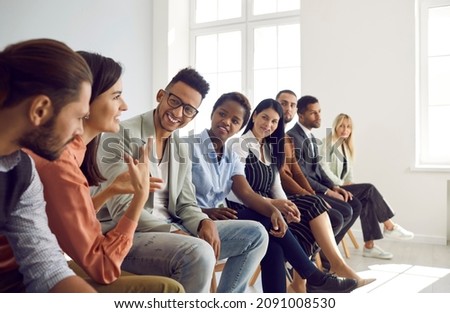 Diverse group of young people sitting in row in modern office and talking. Happy multi-racial men and women having interesting discussion during business meeting or psychological training Royalty-Free Stock Photo #2091008530