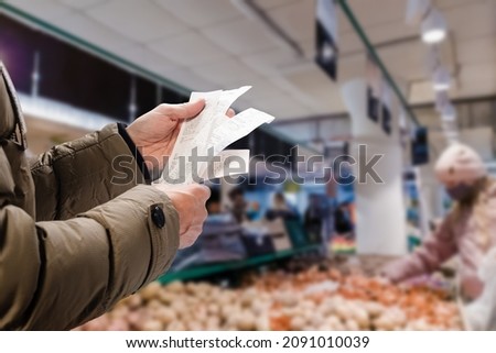 Minded man viewing receipts in supermarket and tracking prices Royalty-Free Stock Photo #2091010039