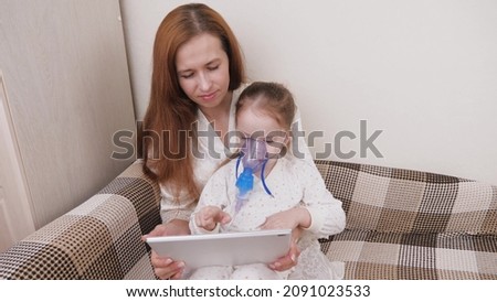 Treat your child for colds at home. Mom treats her daughter with inhalation, and together they watch cartoons on the tablet. The child is receiving respiratory therapy with a nebulizer. Treat cough