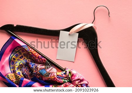 Clothes tag, blank label mockup template for your design. Blank ethic on a black wooden hanger and a silk shawl on a pink background. Advertising banner for clothing boutique Royalty-Free Stock Photo #2091023926