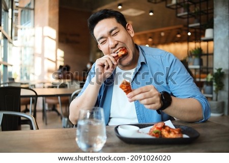 Happy  Asian man eating BBQ chicken wings in restaurant. Royalty-Free Stock Photo #2091026020