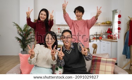 happy family of four smiling at camera with thumb and victory hand gestures while taking burst photos in a modern house interior with chinese new year decorations